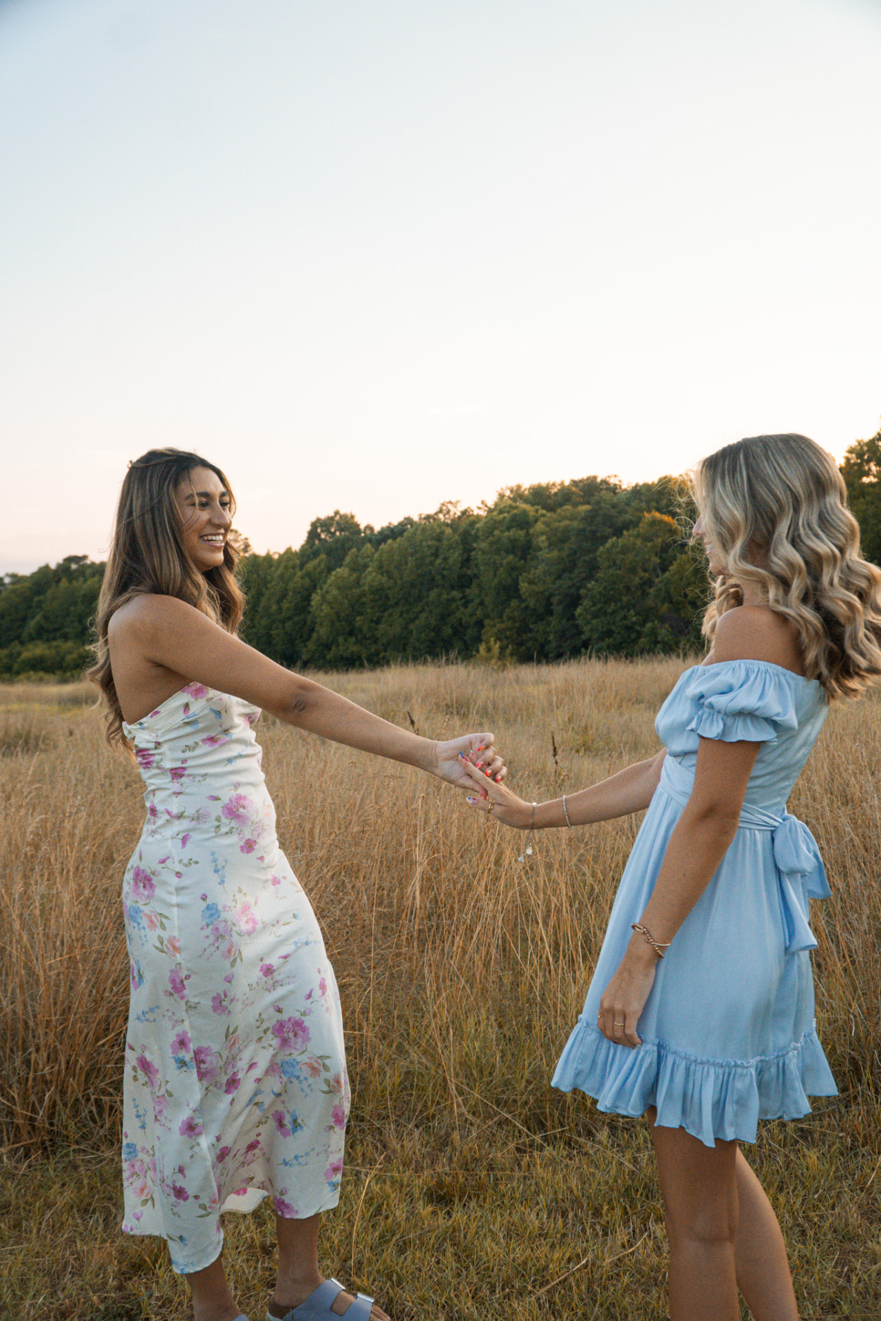 Two friends holding hands in a field at sunset